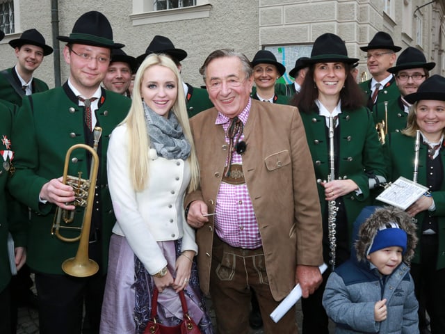 Richard Lugner mit Gattin umringt von Musikern in Trachten gekleidet.