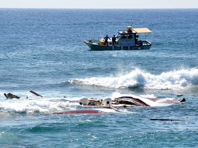 Fischer auf ihrem Boot schauen auf Wrackteile im Wasser