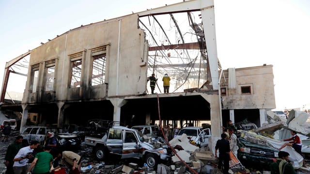 Zerstörte Halle in Sanaa, davor kaputte Autos und Helfer