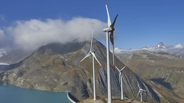 Vier Windturbinen stehen in der Berglandschaft. 