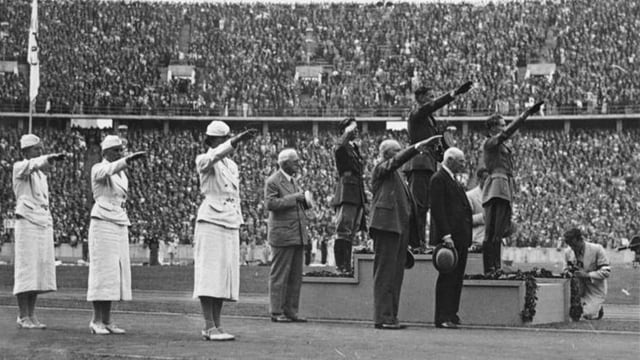 Schwarzweiss-Bild einer Siegerehrung, mehrere Menschen zeigen den Hitlergruss.