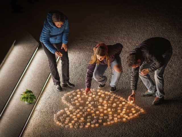 Menschen zünden Kerzen an und stellen sie in Herzform auf.