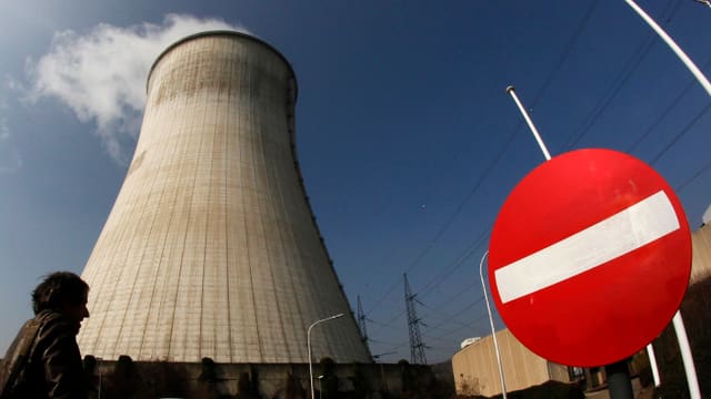 Rauchender Kühlturm des AKWs Tihange in Belgien, mit einem Verbotene-Fahrtrichtung-Verkehrsschild davor.