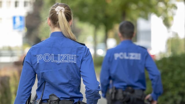 Eine Frau und ein Mann in Polizeiuniform von hinten.