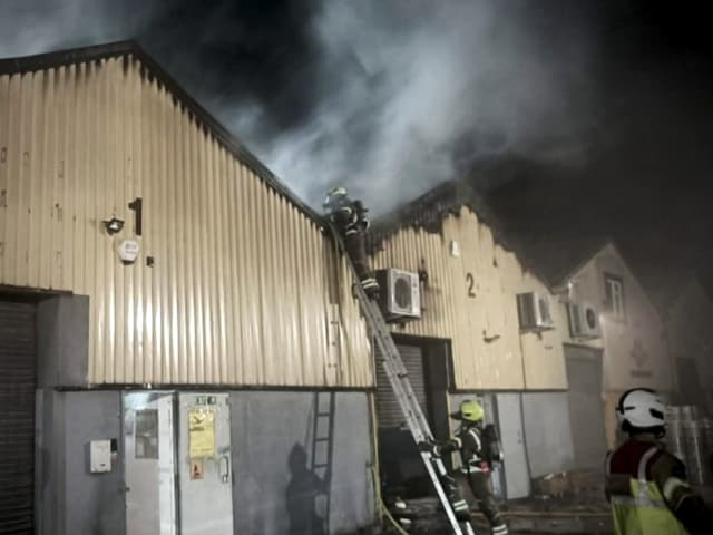 Feuerwehr löscht brennendes Lagerhaus bei Nacht.