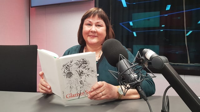 Frau mit Sagenbuch in der Hand sitzt im Radiostudio.