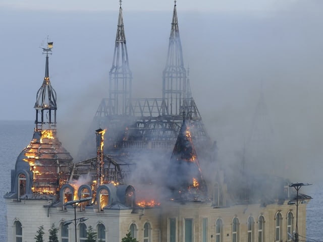 Gotisches Gebäude mit brennendem Dach und Türmen vor nebligem Hintergrund.