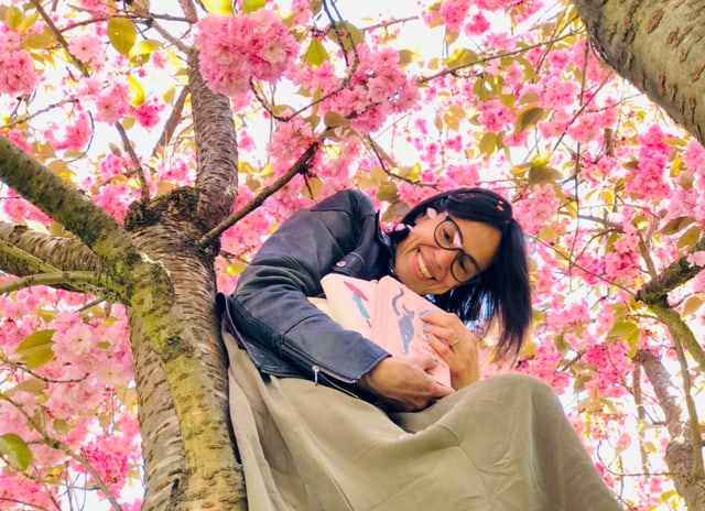 Annette König sitzt auf einem Kirschbaum mit einem Bücherstapel