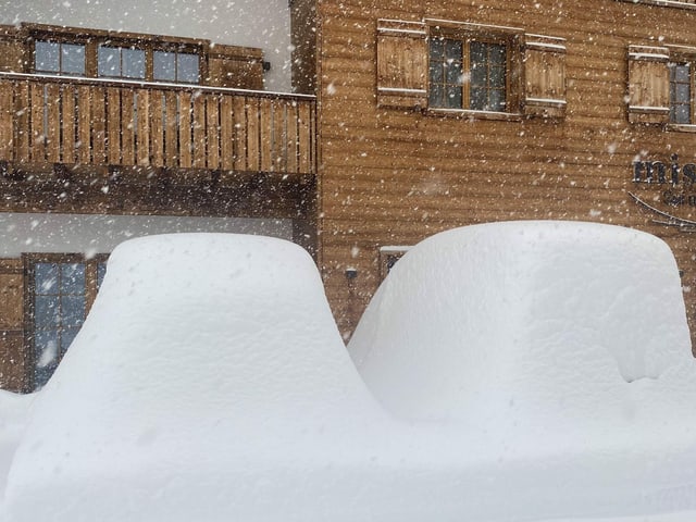 Snow covered cars in front of a chalet.