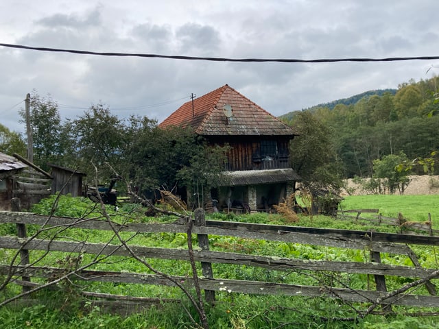 Braunes Haus steht hinter einem braunen Zaun auf einer grünen Wiese.