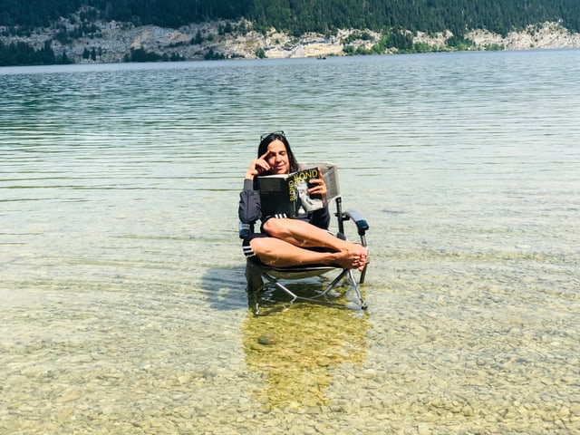 Annette König sitzt auf einem Klappstuhl im Lac de Joux. Dazu liest sie «Blond» von Joyce Carol Oates