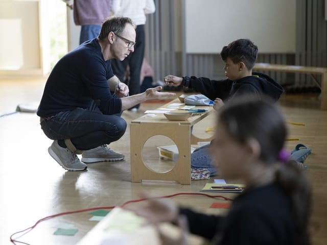 Ein Lehrer spielt mit einem Kind an einer hölzernen Theke. 