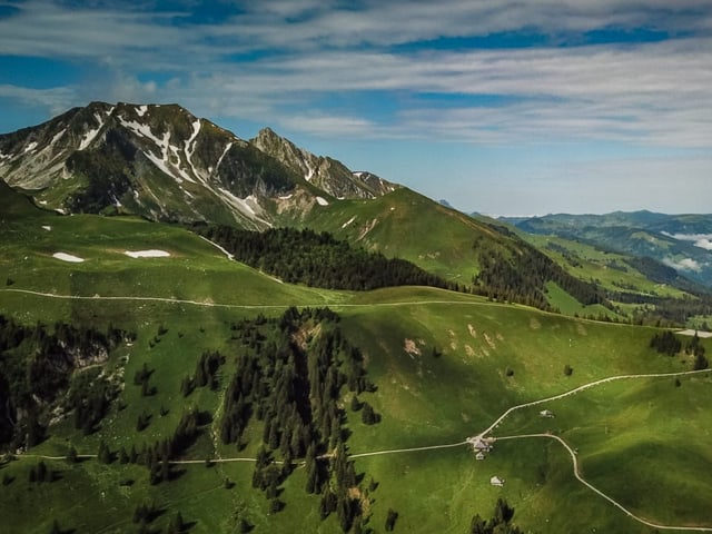 Schöner Blick auf die grünen Weiden der Alp Nünenen, blauer Himmel, ein paar Schleierwolken.