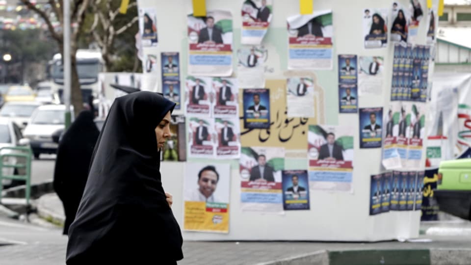Eine Frau läuft in Teheran an Wahlkampfplakaten vorbei.