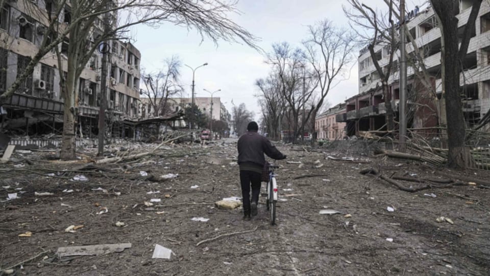 Ein Mann läuft mit seinem Fahrrad auf einer Strasse in Mariupol, die von Raketen getroffen wurde.