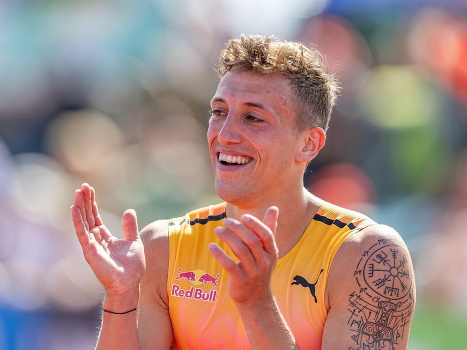Athlet in gelbem Trikot klatscht und lächelt.