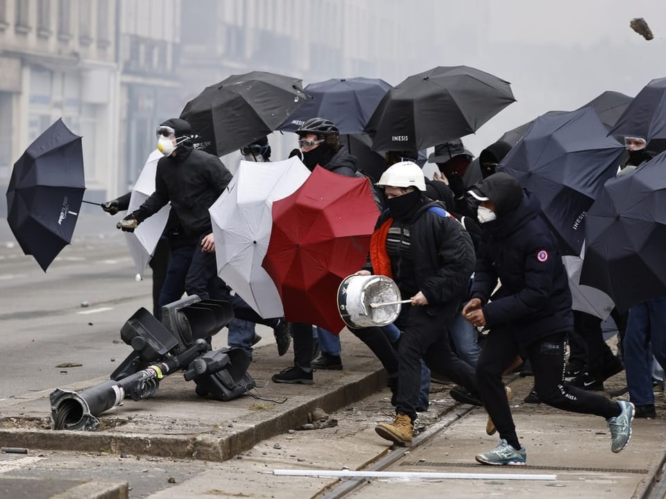 Demonstrierende schützen sich mit Regenschirmen gegen Geschosse.