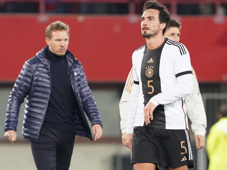 Fussballspieler in weiss-schwarzem Trikot und Trainer auf dem Spielfeld.