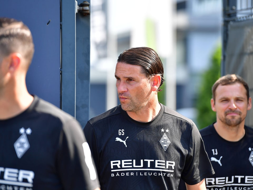 Trainer und Teammitglieder in schwarzen Borussia Mönchengladbach-Trikots.