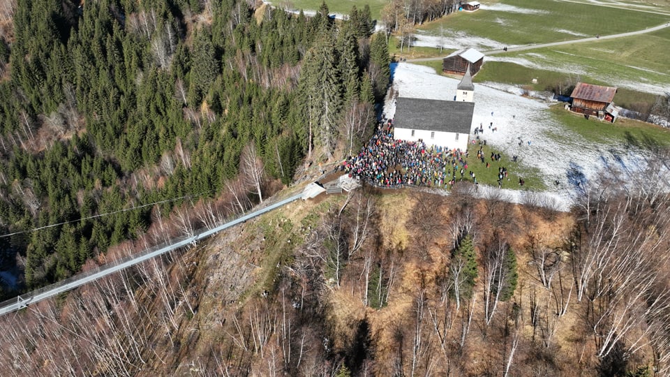 Luftaufnahme einer Kirche im Wald mit Menschenansammlung.