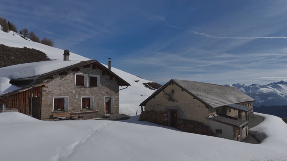 Zwei Berghütten im Schnee vor Berglandschaft.