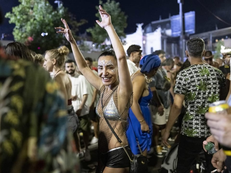 Raverin bei Streetparade in der Nacht, sie streckt die Arme in die Höhe.