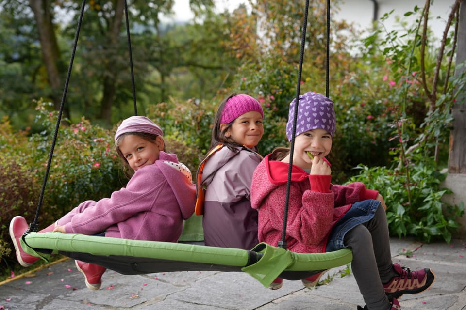 Drei Kinder auf einer Schaukel im Freien.