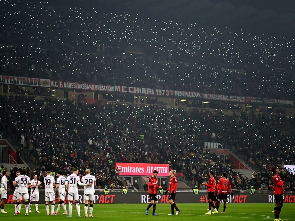 Spieler stehen auf dem Feld, auf der Tribüne leuchten tausende Handy-Taschenlampen