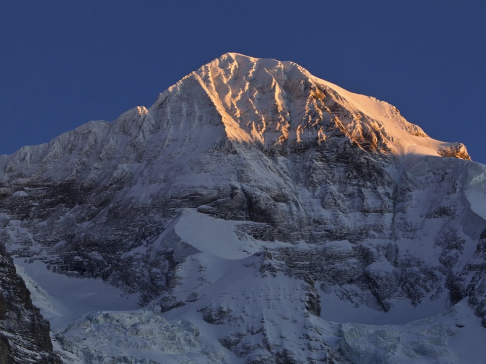 Der Gipfel des Mönchs im Berner Oberland leuchtet im Sonnenlicht.