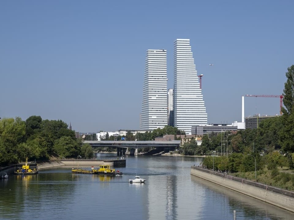 Blick auf den Rhein mit Bauschiffen und auf Basel mit den Roche-Türmen von der Kraftwerkinsel aus in Birsfelden.