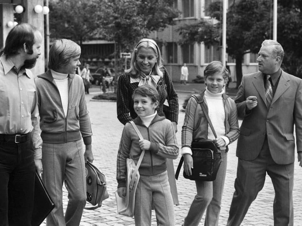 Brigitte Beckenbauer und ihre drei Söhne gehen lächelnd mit einigen Männern eine Strasse in Sarnen entlang.