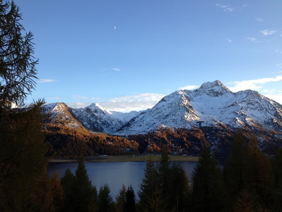 Verschneite Berge und Wald im Sonnenuntergang am See.