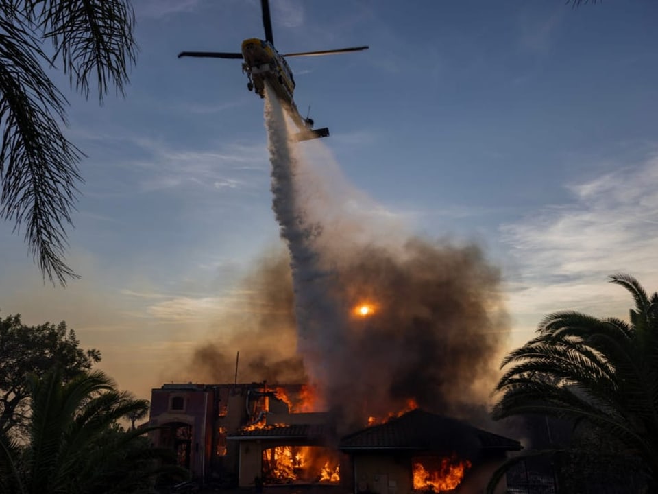 Hubschrauber wirft Wasser auf brennendes Gebäude.