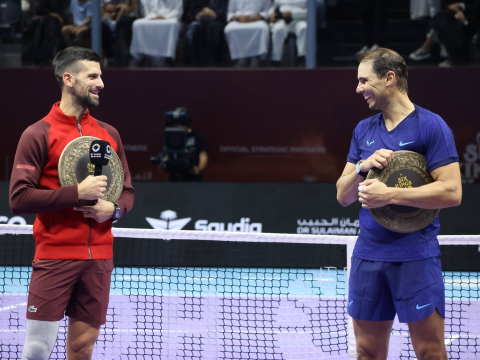 Zwei Tennisspieler halten Trophäen und lächeln sich an.