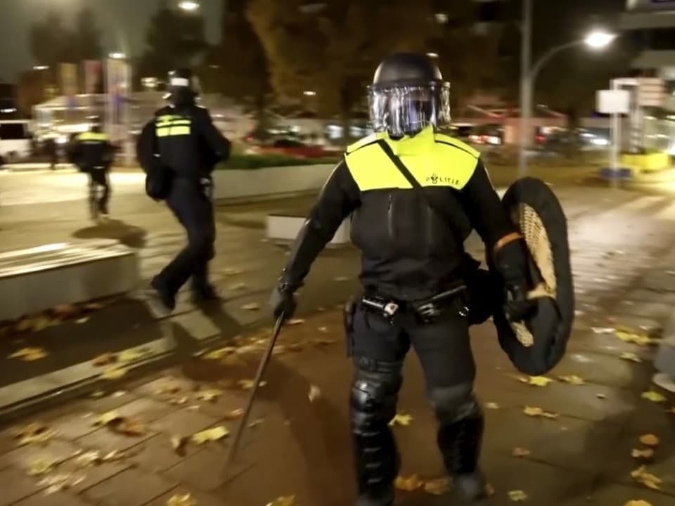 Polizist in Schutzkleidung mit Schild und Schlagstock bei Nacht auf der Strasse.