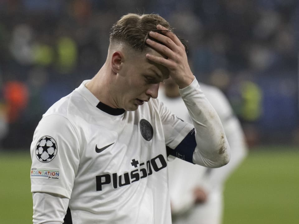 Fussballspieler im weissen Trikot mit der Hand am Kopf auf dem Spielfeld.