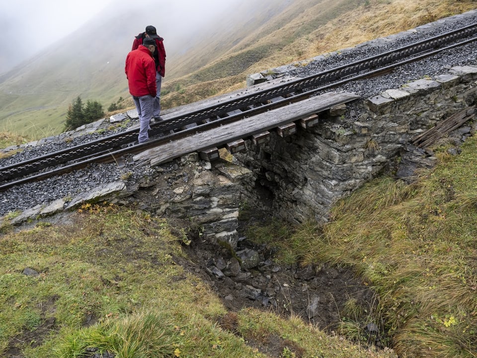 Eine Steinbrücke, darüber ein Gleis, auf dem zwei Männer stehen.