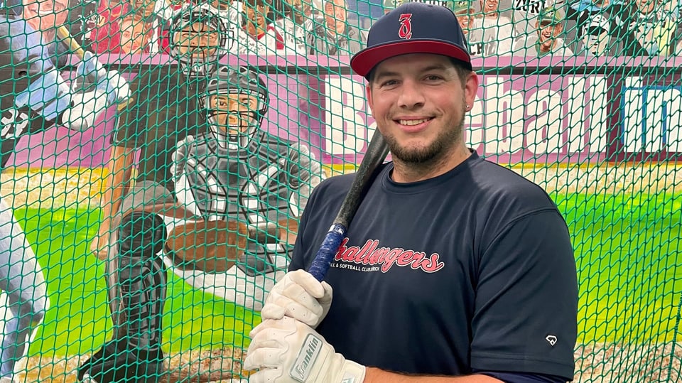 Marco Limacher trägt eine dunkelblaue Kappe und ein  T-Shirt von seinem Club, er hält einen Baseball-Schläger.