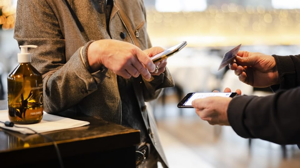 Eine Person streckt sein Handy und einen Personalausweis einer anderen Person mit Handy entgegen.