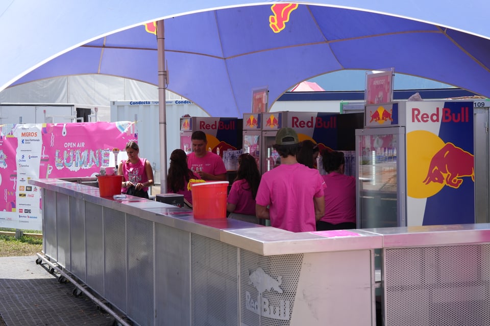 Festival-Verkaufsstand mit Red Bull-Logo und Team in pinken T-Shirts am Open Air Lumnezia 2024.