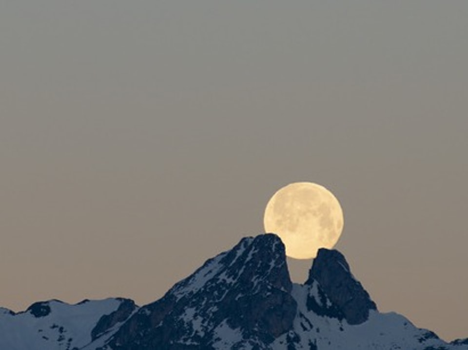 Auf dem Bild ist der Mond hinter einer Bergkette zu sehen.