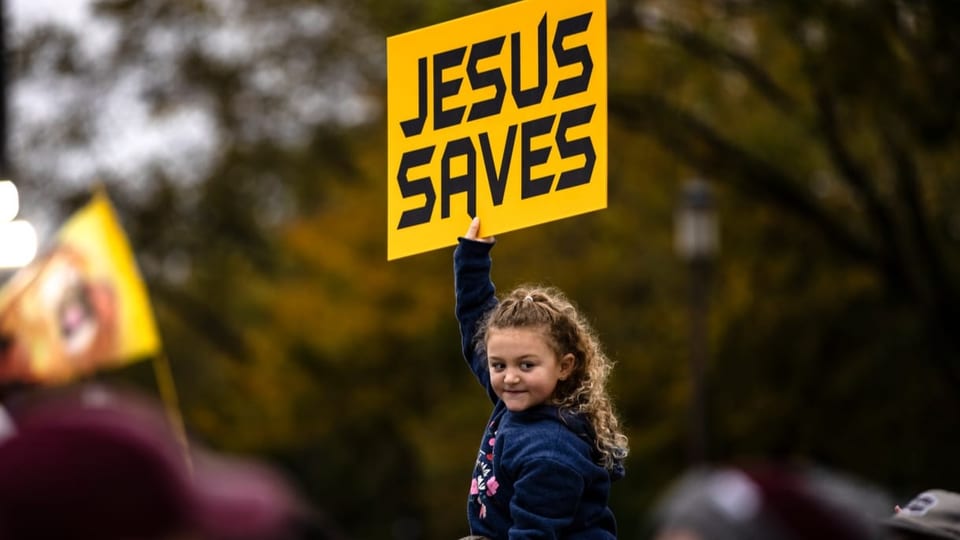 Ein Mädchen hält ein gelbes Schild in die Luft mit der Aufschrift «Jesus saves».
