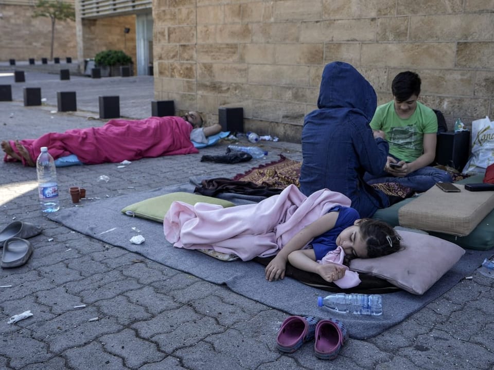 Menschen schlafen auf dem Bürgersteig mit Decken und Kissen.