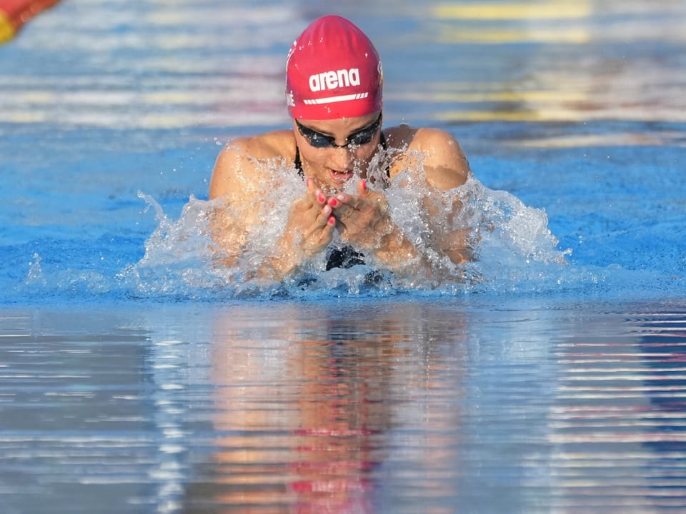 Schwimmer mit roter Kappe beim Brustschwimmen im Wasser.