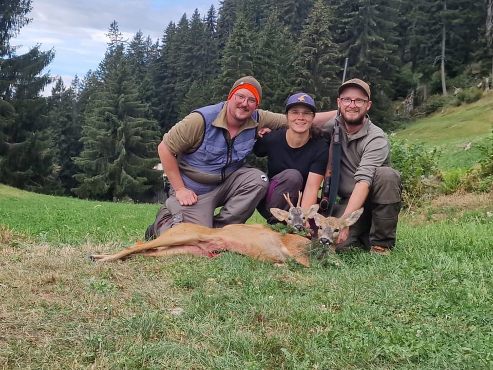 Drei Personen posieren mit einem erlegten Reh im Wald.