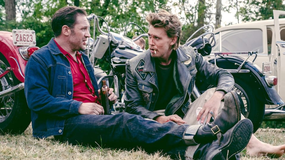 Zwei Manner in Jeans und Leder-Kluft sitzend vor Motorrädern.