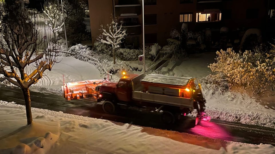 Schneepflug räumt nachts verschneite Strasse.