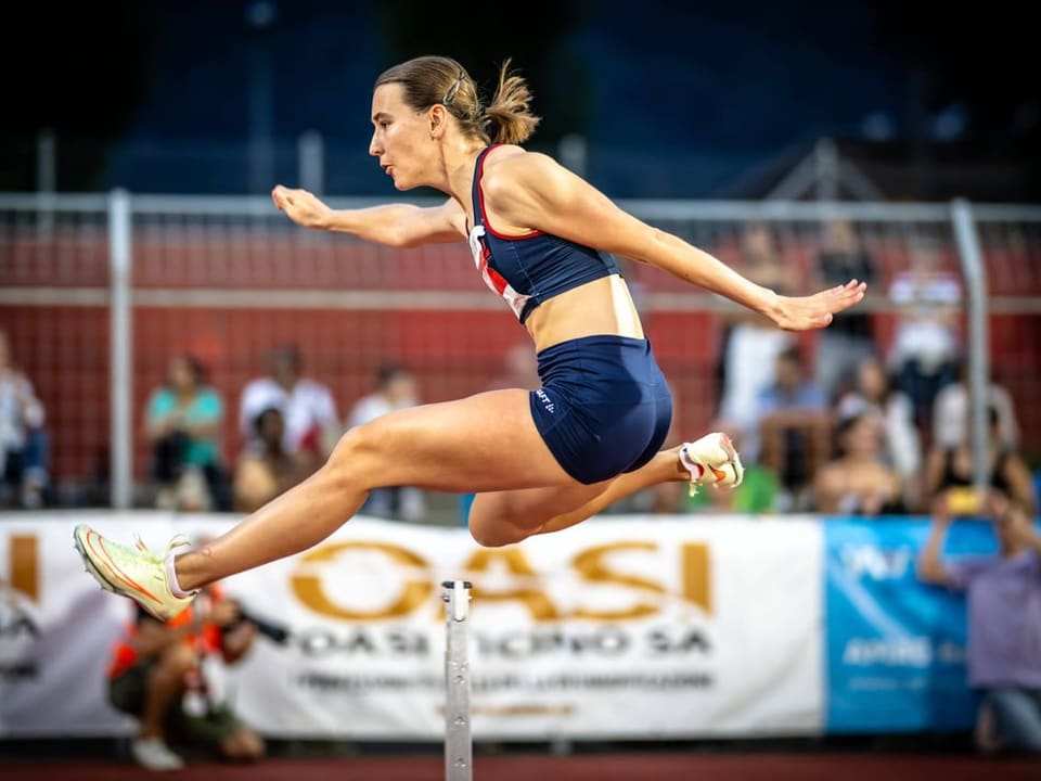 Weibliche Athletin springt bei einem Leichtathletik-Wettkampf über ein Hindernis.