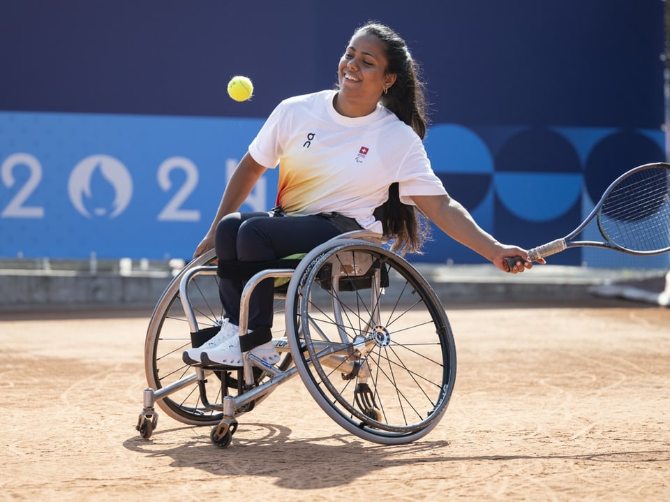 Rollstuhl-Tennisspielerin beim Rückschlag auf dem Platz.