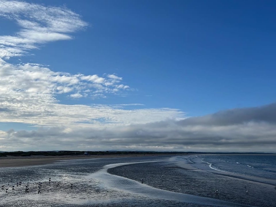 Strand mit Wolken und blauem Himmel.